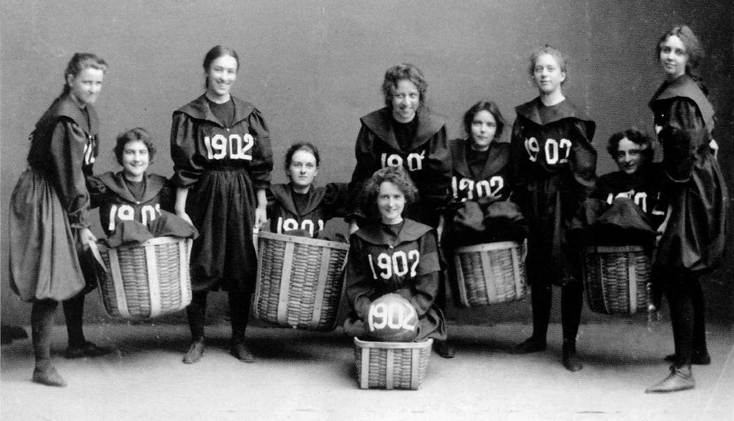 The Smith College class of 1902 basketball team posed in bloomers and middy blouses, holding woven peach baskets and a ball marked 1902.