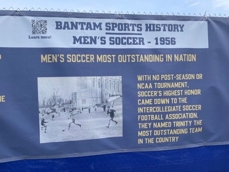 Bantam Sports History windscreen banner along the construction fence, featuring Men's Soccer 1956 — 'Most Outstanding in Nation.'